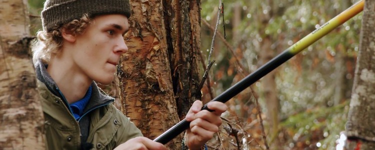 En ung man med skogsgröna kläder håller i ett fiskespö. Foto: Bitzer Productions AB
