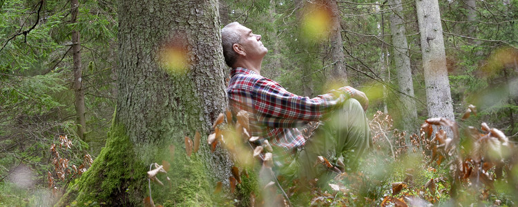 Man som sitter lutad mot en gran i skogen.  Foto: @ Camilla Zilo