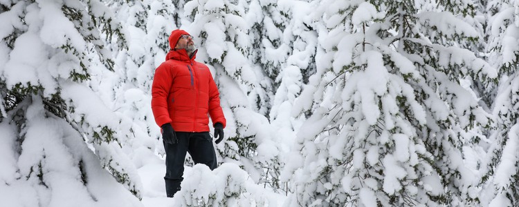 Man i röd dunjacka och mössa står mitt inne bland snötäckta granar. Ett riktigt vinterlandskap. Foto: André Nyström