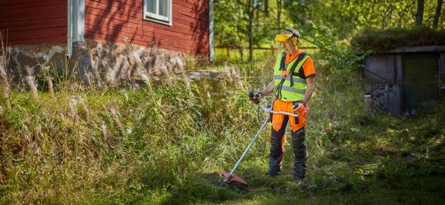 Man med röjsåg, i bakgrunden syns en röd stuga. Foto: Patrik Svedberg