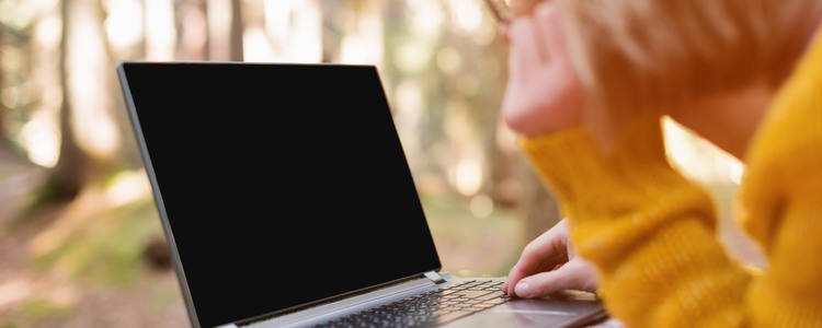 Närbild på kvinna som använder sin laptop i skogen. Foto: Mostphotos