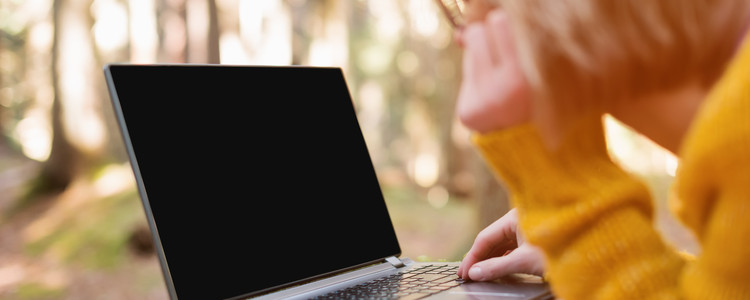 Närbild på kvinna som använder sin laptop i skogen. Foto: Mostphotos