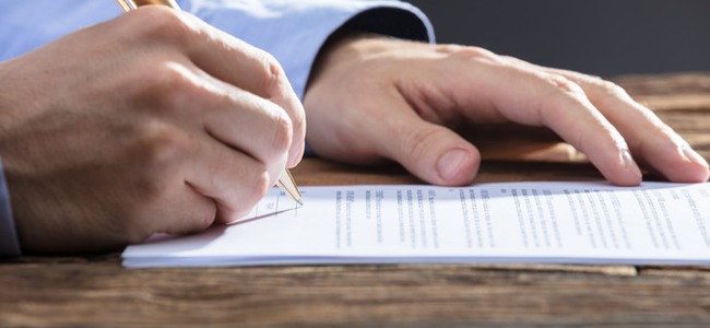 Close-up Of A Businesspersons Hand Signing Document On Wooden Desk. Foto: Andrey Popov