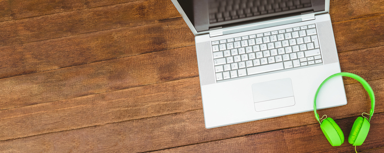 View of a grey laptop with a green headphone on wood desk. Foto: Wavebreak Media LTD