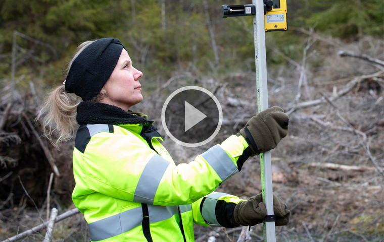 Kvinna i varselkläder med mätinstrument i skogen.