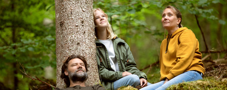 Familj som myser i skogen lutade mot trädstam. Foto: @ Camilla Zilo