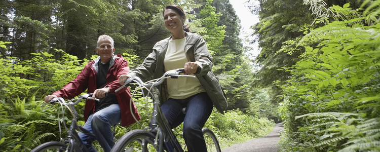 Medelålders man och kvinna cyklar i skogen. Glada och lyckliga i sommarsolen. Foto: MostPhotos