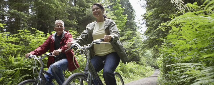 Medelålders man och kvinna cyklar i skogen. Glada och lyckliga i sommarsolen. Foto: MostPhotos