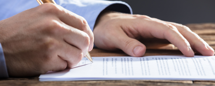 Close-up Of A Businesspersons Hand Signing Document On Wooden Desk. Foto: Andrey Popov