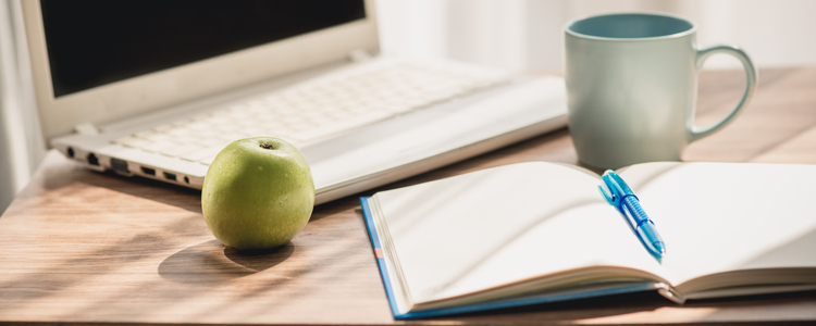 Skrivbord med laptop, ett grönt äpple, penna och papper.