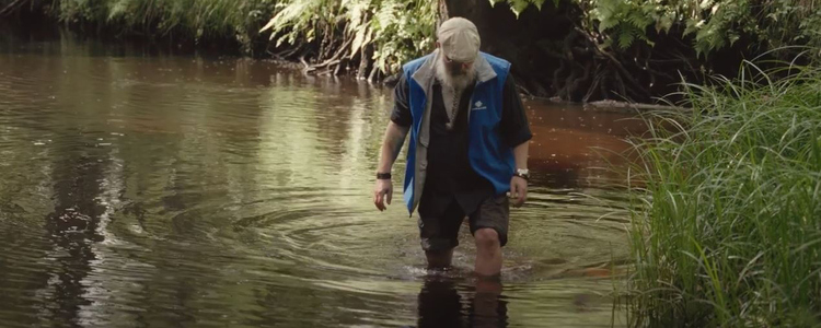 En man klädd i blå Grip on Life-väst står i ett vattendrag. Bild från filmserien Levande vattendrag.