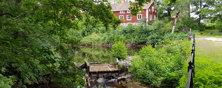 Summer environment from Järle Kvarn with rushing river, lush trees and older red houses with white knots