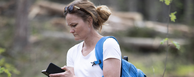 Kvinna står i skogen och tittar på mobilen. 
